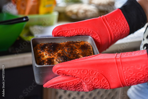 a woman in red silicone gloves holds bread in a mold baked in a home kitchen