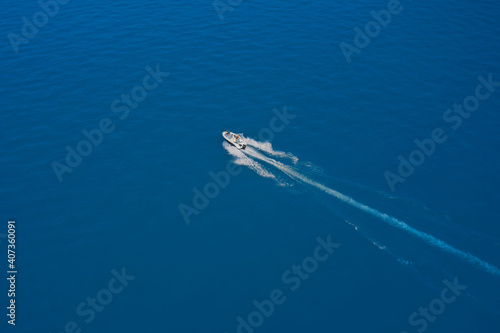 Top view of a white boat sailing to the blue sea. High-speed boat of white color fast motion on blue water in the rays of the sun top view. Travel - image. Aerial view luxury motor boat.