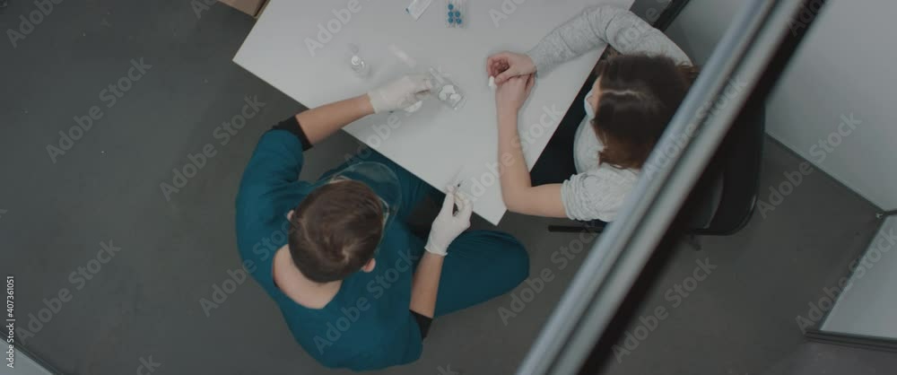 OVERHEAD HIGH ANGLE Caucasian male doctor wearing face shield and mask preparing to administer the vaccine to a patient inside temporary vaccination cabin. COVID-19 coronavirus vaccination OVERHEAD HIGH ANGLE Caucasian male doctor wearing face shield and mask preparing to administer the vaccine to a patient inside temporary vaccination cabin. COVID-19 coronavirus vaccination