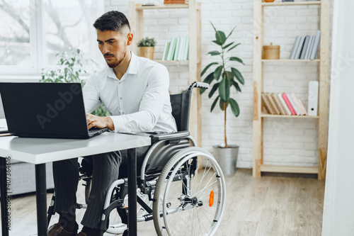 Quadro em tela Serious concentrated man in wheelchair using his laptop for work / seeking a job