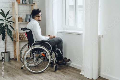 Young disabled man sitting in a wheelchair near the window