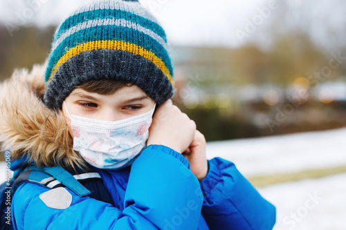 Kid boy wearing ffp medical mask on the way to school. Child backpack satchel. Schoolkid on cold autumn or winter day with warm clothes. Lockdown and quarantine time during corona pandemic disease