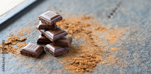 Broken pieces of chocolate and cocoa powder on a wooden background