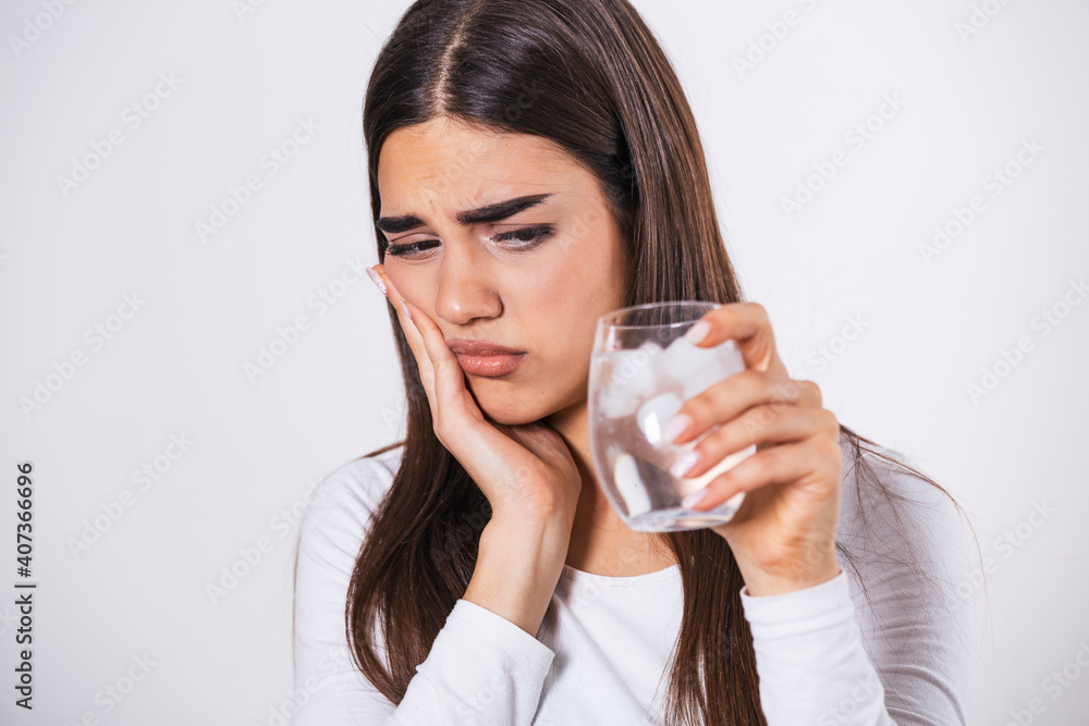 Young woman with sensitive teeth and hand holding glass of cold water with ice. Healthcare concept. woman drinking cold drink, glass full of ice cubes and feels toothache, pain Young woman with sensitive teeth and hand holding glass of cold water with ice. Healthcare concept. woman drinking cold drink, glass full of ice cubes and feels toothache, pain