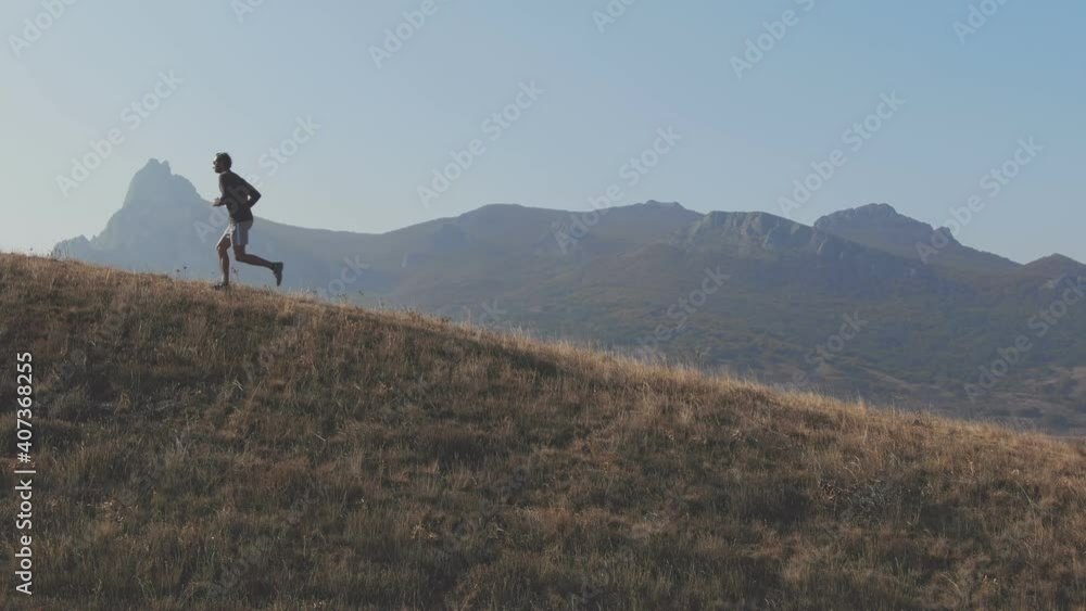 Man is running up to hilltop from right to left. Scene is showing a mountain peak background and hill edge in that appears the running man Man is running up to hilltop from right to left. Scene is showing a mountain peak background and hill edge in that appears the running man