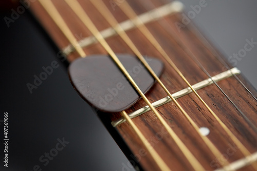 leisure, music and musical instruments concept - close up of bass guitar neck with pick between strings