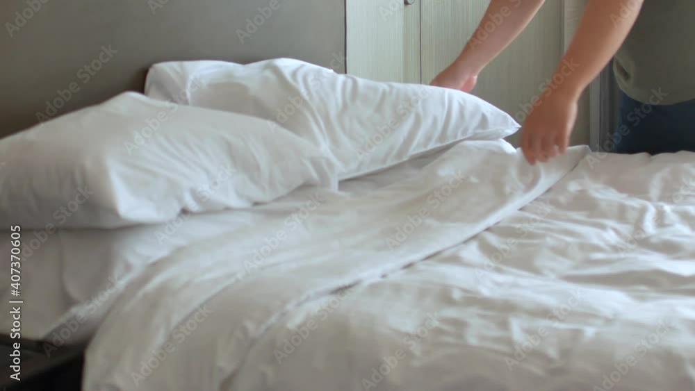 Housekeeper is making the bed in the room- place pillow into the bed Housekeeper is making the bed in the room- place pillow into the bed