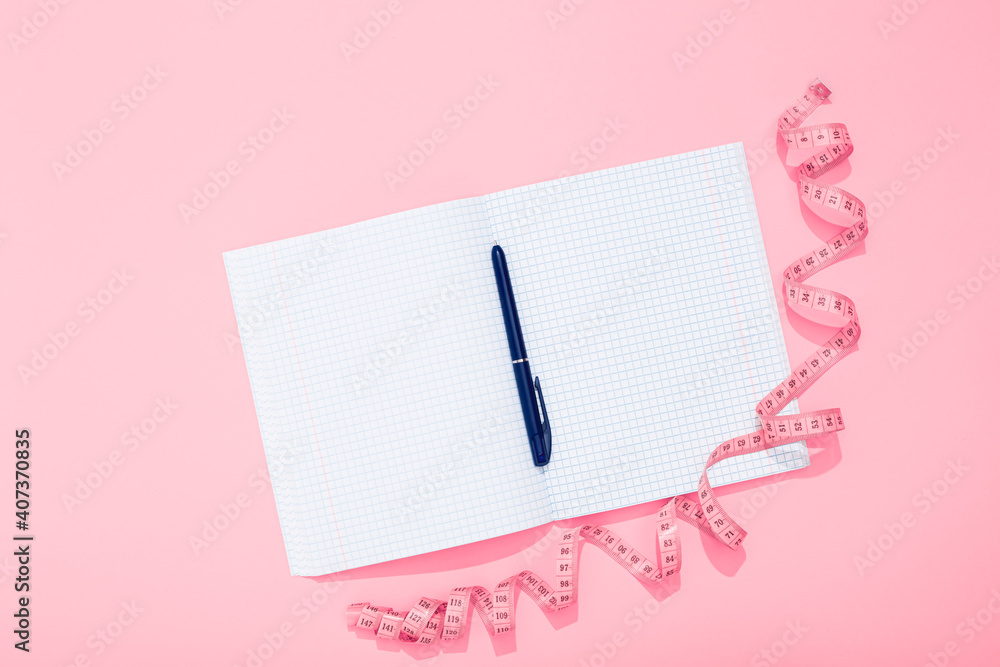 Twisted centimeter tape and clean note book and blue pen with copy space on pink background. Greeting postcard. Body measurement. Nutrition and fitness workout plan. International Women Day 8 March Twisted centimeter tape and clean note book and blue pen with copy space on pink background. Greeting postcard. Body measurement. Nutrition and fitness workout plan. International Women Day 8 March