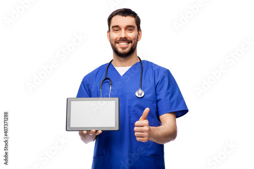 medicine, healthcare and technology concept - happy smiling doctor or male nurse in blue uniform with stethoscope and tablet pc computer showing thumbs up over white background