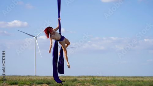 Professional aerial gymnast circus artist on red bright aerial silks performs a graceful pose