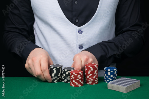 a croupier in a white vest and a black shirt is counting poker chips