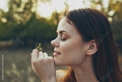 beautiful woman holds a praying mantis on her hand in nature on a meadow in summer