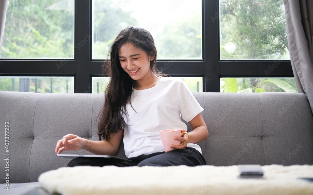 Smiling young woman sitting on comfortable sofa and using digital tablet.