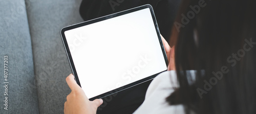 Fototapeta Naklejka Na Ścianę i Meble -  Close up view of casual young woman sitting on comfortable sofa and using digital tablet with blank screen.
