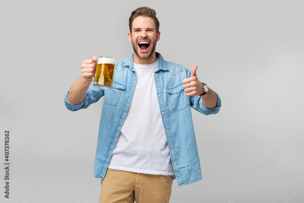 Young Man holding wearing jeans shirt holding glass of beer standing over Grey Background Young Man holding wearing jeans shirt holding glass of beer standing over Grey Background