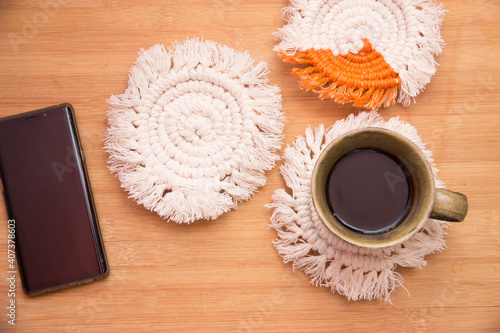 Top View black hot coffee in a cup on white macrame coasters with mobliephone