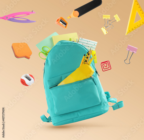 Backpack surrounded by flying school stationery on pale orange background photo