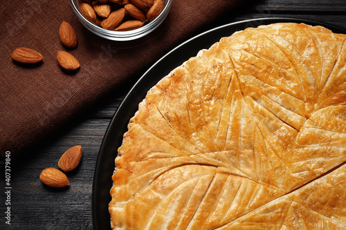 Traditional galette des rois and almonds on black wooden table, flat lay