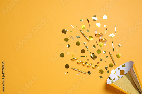 Party cone with shiny confetti on orange background, flat lay. Space for text