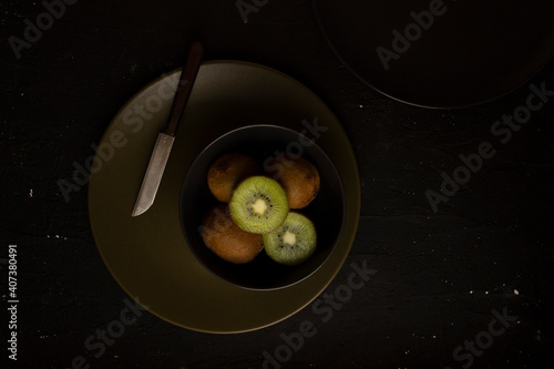Kiwis on a plate isolated on dark black background. Still life photography. Food photography. Sliced kiwi on a plate.
