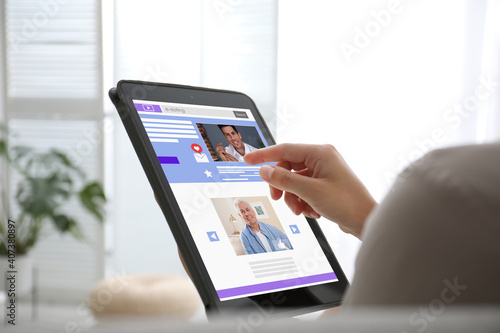 Young woman visiting online dating site via tablet indoors, closeup