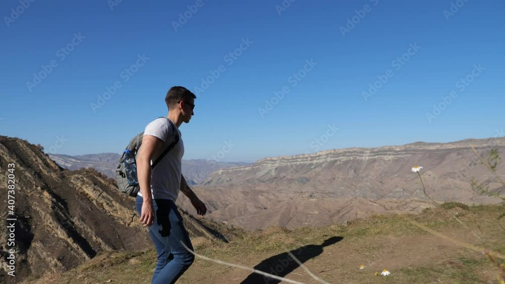 young man with a backpack walks down the slope against the background of mountains on a clear autumn day. young man with a backpack walks down the slope against the background of mountains on a clear autumn day.