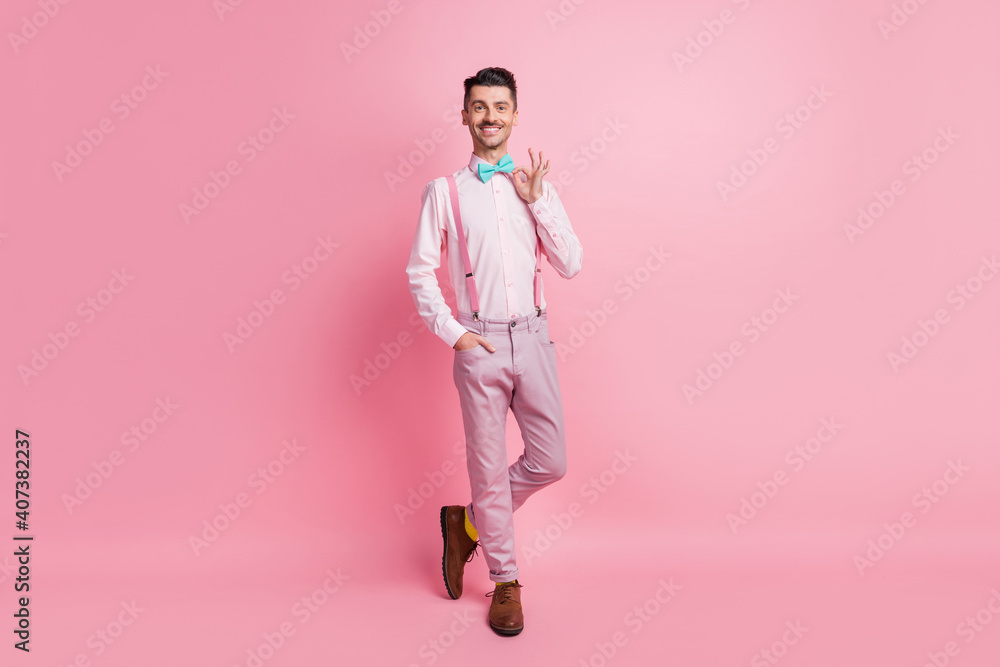 Photo portrait full body view of man adjusting bowtie isolated on pastel pink colored background Photo portrait full body view of man adjusting bowtie isolated on pastel pink colored background
