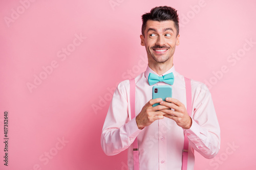 Photo portrait of man looking at blank space holding phone in two hands isolated on pastel pink colored background