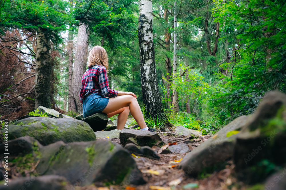 Hipster girl in the mountains. Stylish woman in checkered shirt sitting on stones in forest. Wanderlust concept. Hiking and travelling in summer. Mysterious wood. Beautiful nature. Hipster girl in the mountains. Stylish woman in checkered shirt sitting on stones in forest. Wanderlust concept. Hiking and travelling in summer. Mysterious wood. Beautiful nature.