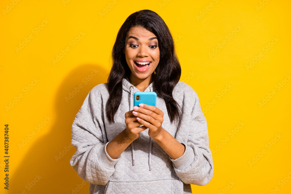 Photo of impressed funny dark skin girl dressed grey sweatshirt typing looking modern gadget isolated yellow color background Photo of impressed funny dark skin girl dressed grey sweatshirt typing looking modern gadget isolated yellow color background