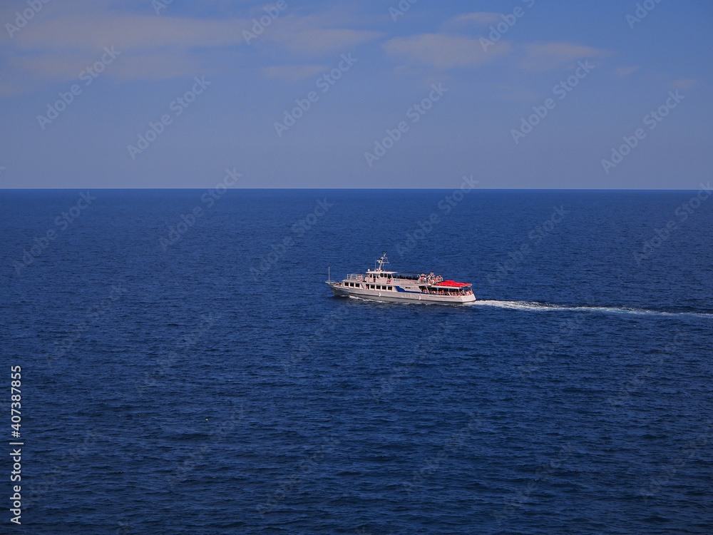 A large beautiful motor ship filled with people glides along the open blue sea to the horizon, leaving a trail of water behind it. Sea voyage on a summer day.