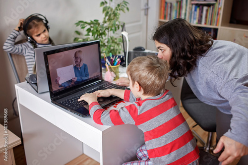 Distant education at home, children doing homework and mother working and help them. Elementary school kids during online class with parent working remotely in one room, self-isolation, quarantine