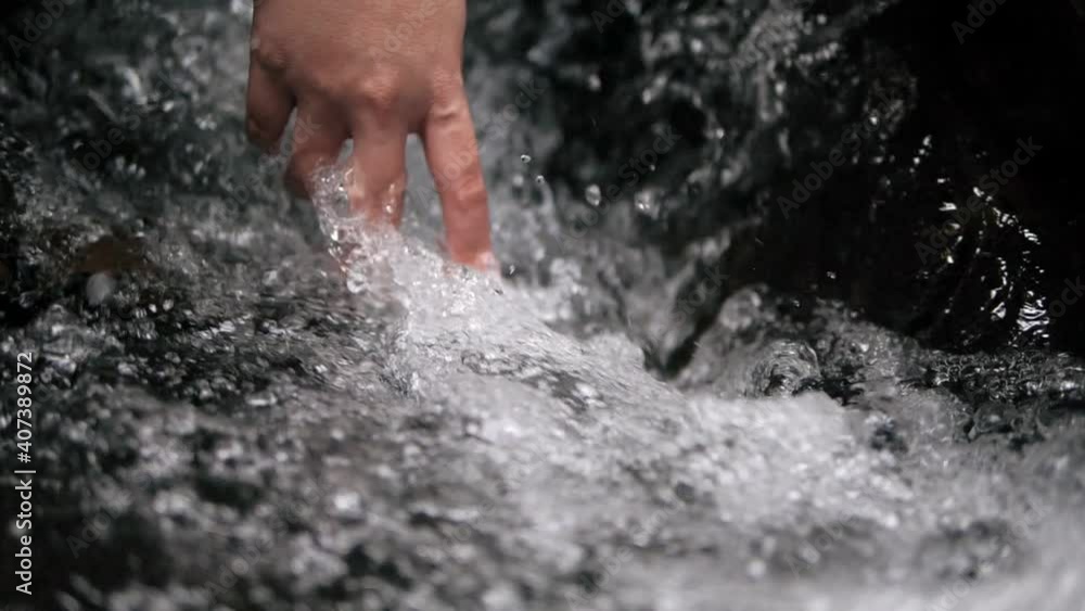 Hand touching clean water splash stream in the rocks at mountain waterfall. Beautiful cascading water of nature forest river. Clear water runs through the stones, Close up Hand touching clean water splash stream in the rocks at mountain waterfall. Beautiful cascading water of nature forest river. Clear water runs through the stones, Close up