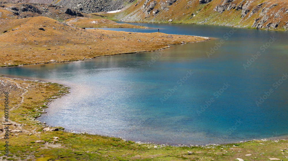 man standing alone looking at natural park lake in mountain environment. colorful blue water. safe isolated location during covid-19 pandemic 
