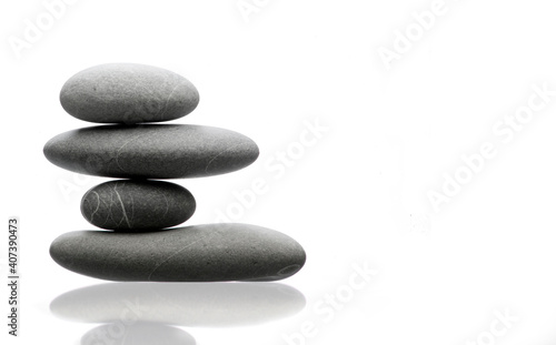 Balanced pile of four grey stones  reflex on white table  equilibrium concept 