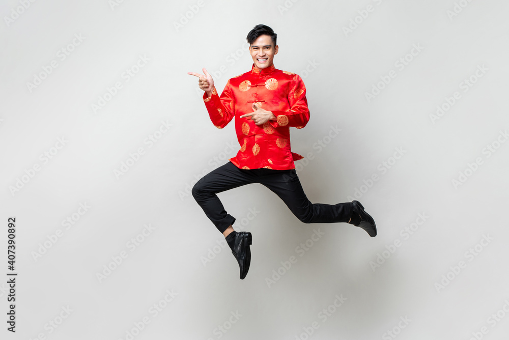 Portrait of smiling handsome Asian man in traditional chinese attire smiling and pointing hands to empty space aside in light gray isolated studio background
