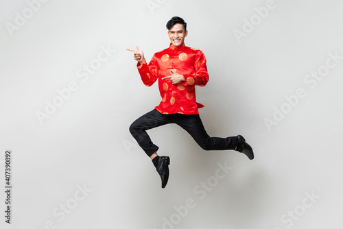 Portrait of smiling handsome Asian man in traditional chinese attire smiling and pointing hands to empty space aside in light gray isolated studio background