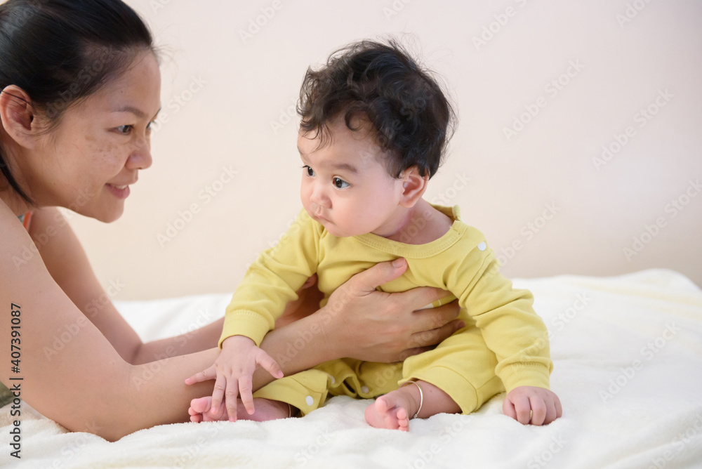 Asian mother tried to hold the cute little baby sitting on the bed Asian mother tried to hold the cute little baby sitting on the bed