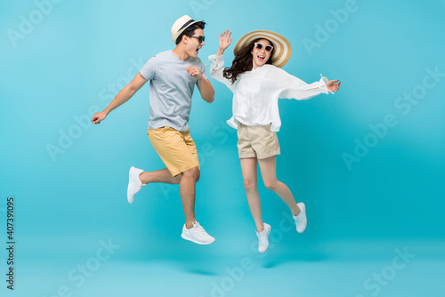 Smiling energetic Asian couple tourists in summer beach casual clothes jumping isolated on light blue studio background
