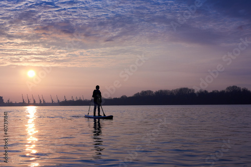 Silhouette of a boy standing on SUP during a beautiful winter sunrise on the river © watcherfox