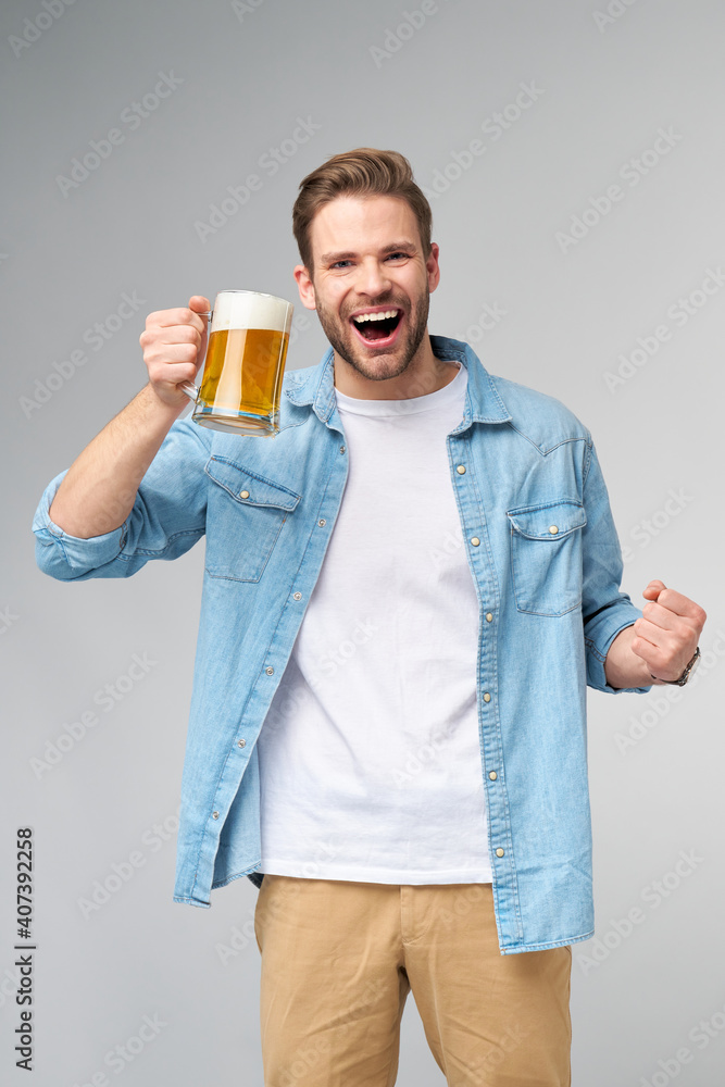 Young Man holding wearing jeans shirt holding glass of beer standing over Grey Background Young Man holding wearing jeans shirt holding glass of beer standing over Grey Background