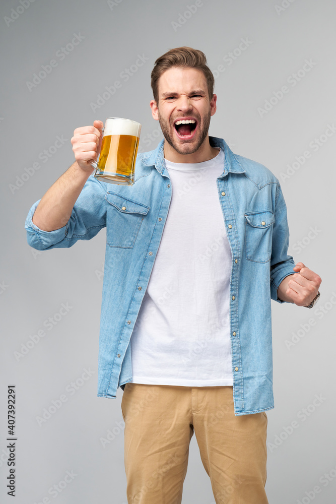 Young Man holding wearing jeans shirt holding glass of beer standing over Grey Background Young Man holding wearing jeans shirt holding glass of beer standing over Grey Background