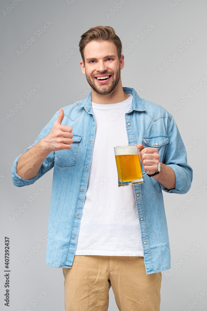 Young Man holding wearing jeans shirt holding glass of beer standing over Grey Background Young Man holding wearing jeans shirt holding glass of beer standing over Grey Background
