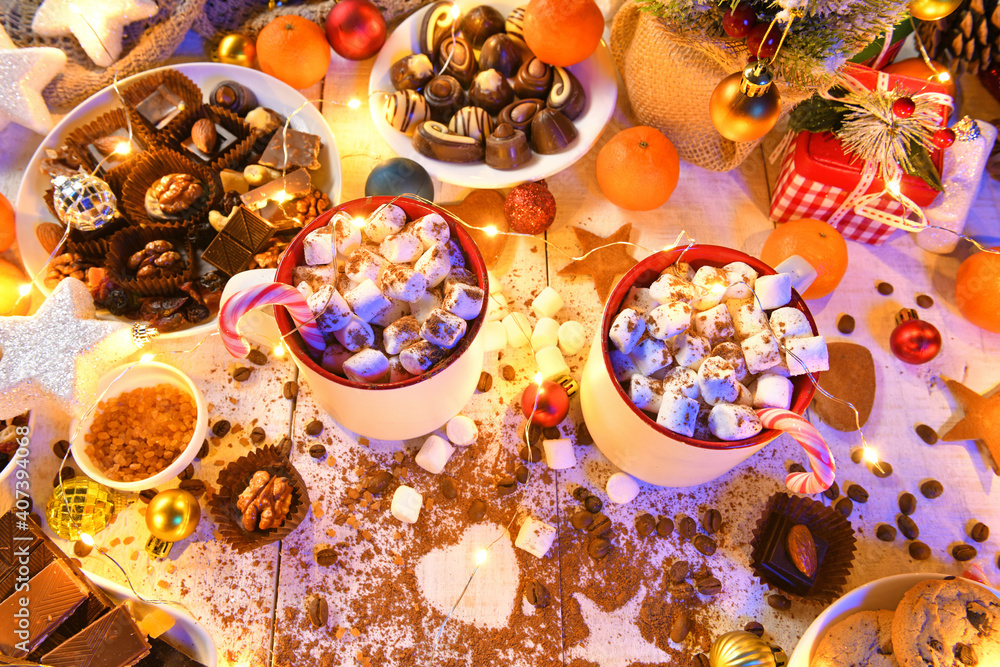sweet food top view background for merry christmas or new year holiday decoration with night illumination - chocolate candies, tangerines, cookies, marshmallow and cocoa latte on white wood