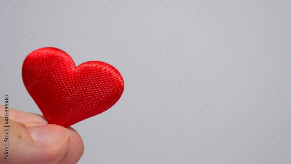 4K: Small red textured heart held with your fingers on a white or gray background: place for text, background for Valentine's day, heart health 4K: Small red textured heart held with your fingers on a white or gray background: place for text, background for Valentine's day, heart health