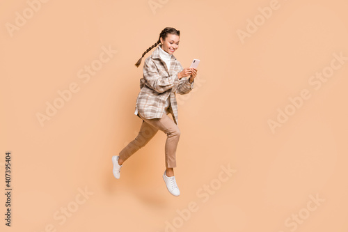 Full size profile side photo of young happy positive girl running in air use smartphone isolated on beige color background