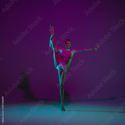 Flexible. Young female athlete, rhythmic gymnastics artist dancing, training isolated on purple studio background in neon light. Beautiful girl practicing with equipment. Grace in performance.
