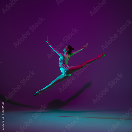 Flying. Young female athlete, rhythmic gymnastics artist dancing, training isolated on purple studio background in neon light. Beautiful girl practicing with equipment. Grace in performance. © master1305