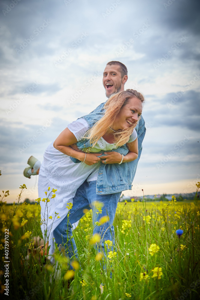 Young beautiful couple having fun on natural background. Date of guy and girl on a green field with glass and flowers in cloudy summer day. Yound family having rest together Young beautiful couple having fun on natural background. Date of guy and girl on a green field with glass and flowers in cloudy summer day. Yound family having rest together