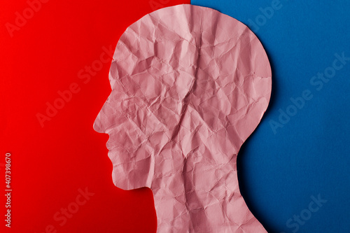 Head silhouette made of paper. Crumpled pink paper shaped as a human head with copy space on red and blue paper background. photo